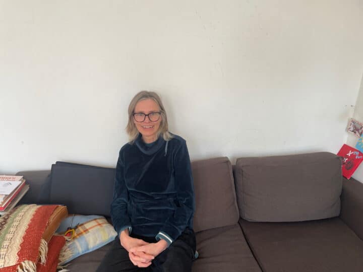 Huurder Ymere Amsterdam zit op bank in woning, glimlacht, comfortabele sfeer.